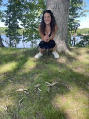 A woman posing next to a tree in the grass