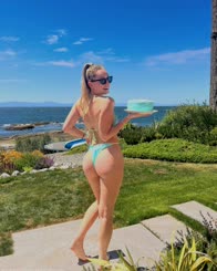 A bikini model posing with a cake in hand on a beach